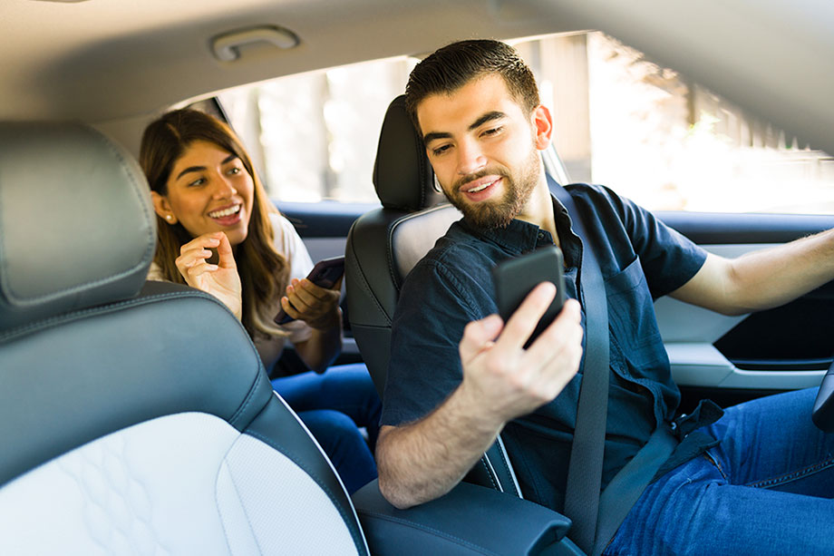 Foto mostra motorista de Uber e passageira, os dois com o celular em mãos