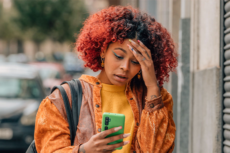 Foto de mulher jovem olhando para o celular com semblante assustado, como quem descobriu ter caído em um golpe