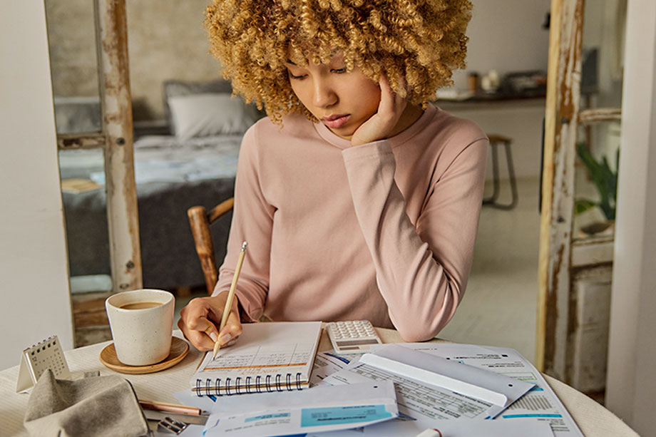 Foto mostra mulher fazendo contas em um bloquinho, ao lado de uma calculadora
