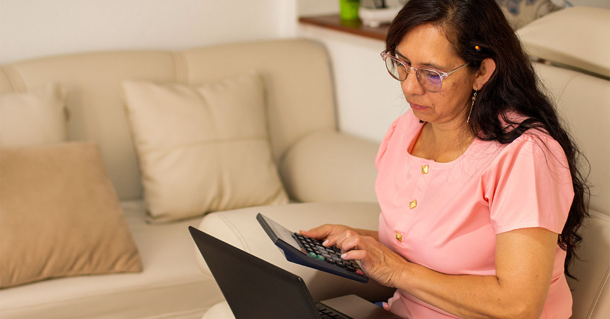 Foto de mulher fazendo contas na calculadora e com laptop no colo