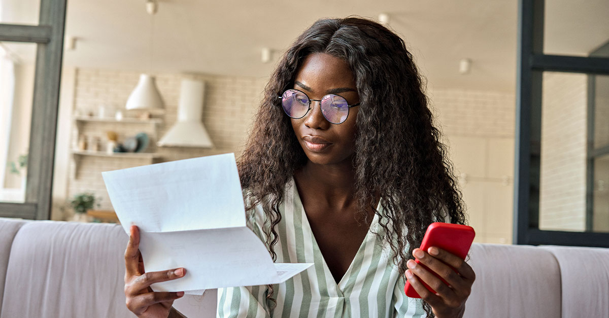 Foto de mulher consultando um papel com o celular na outra mão