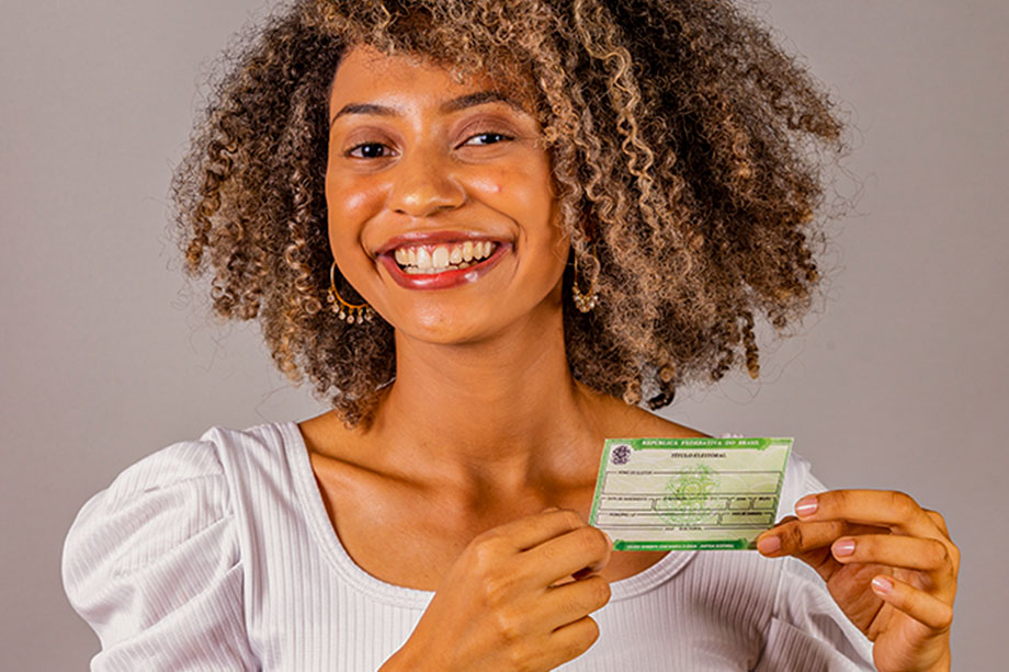 Foto mostra mulher sorridente segurando um documento pessoal