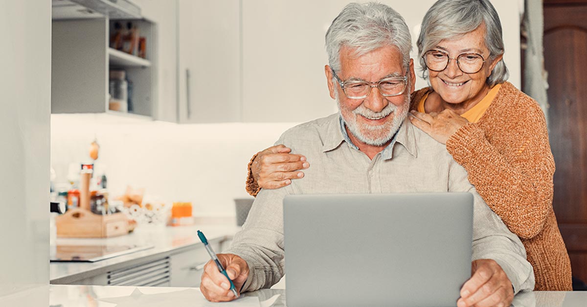 Casal de idosos olhando computador e sorrindo.